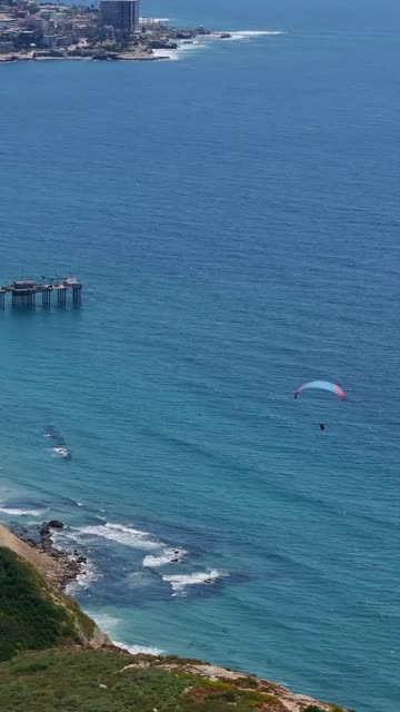 Aerial view of the cliffs, the pier and boats at Black’s Beach, with a crowd gathered.