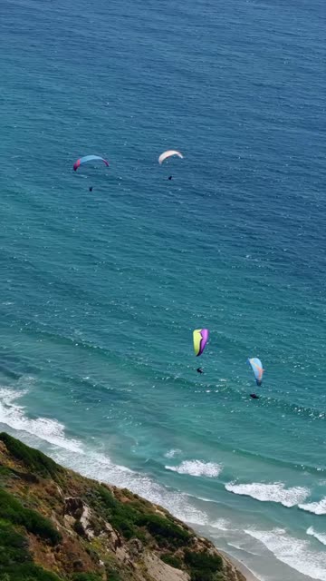 Aerial view of the cliffs, the surf and the ocean at Black’s Beach, with a crowd gathered.