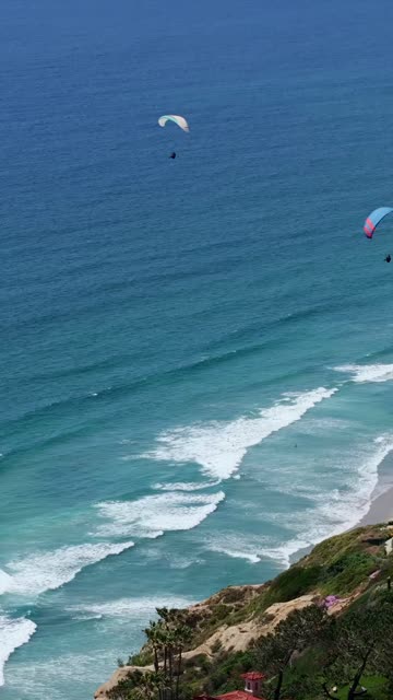 Elevated view of the cliffs, the surf and the ocean at Black’s Beach, with a crowd gathered.