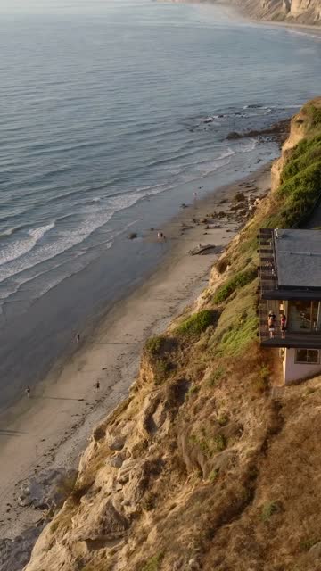 Aerial view of the cliffs, the ocean and the buildings at Black’s Beach, with people walking.