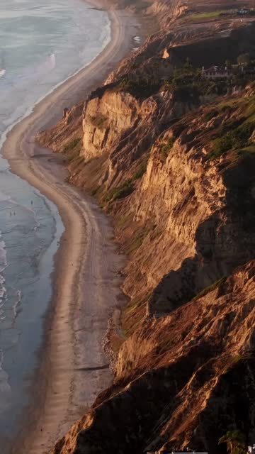 Aerial view of the cliffs, the ocean and the beach at Black’s Beach, with people walking.