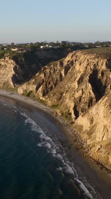 Aerial view of the cliffs, the ocean and homes at Black’s Beach, with people walking.