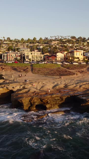Low aerial view of the cliffs, palm trees and the ocean at Sunset Cliffs, with people walking.