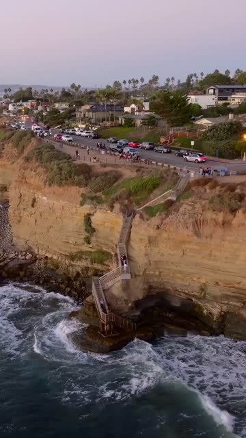 Aerial view of the cliffs, the surf and palm trees at Sunset Cliffs, with a crowd gathered.