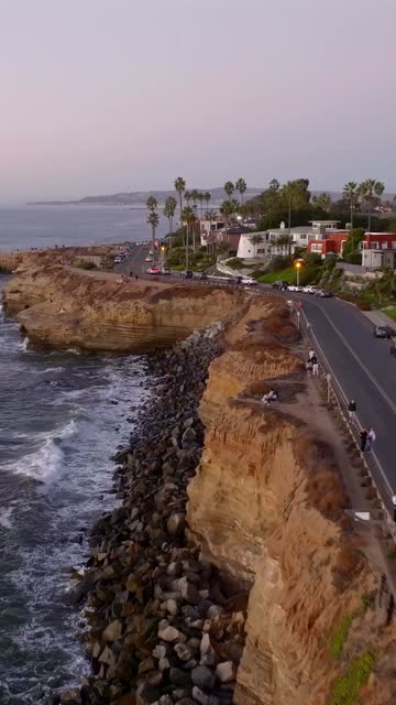 Low aerial view of the cliffs, the surf and palm trees at Sunset Cliffs, with people walking.