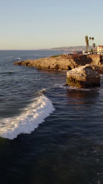 Low aerial view of the cliffs, the surf and palm trees at Sunset Cliffs.