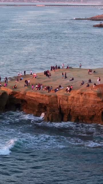 Aerial view of the cliffs, the surf and the ocean at Sunset Cliffs, with a crowd gathered.