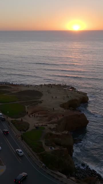 Aerial view of the cliffs, the ocean and traffic at Sunset Cliffs, with a crowd gathered.
