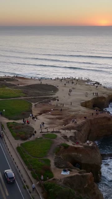 Aerial view of the cliffs, the surf and the ocean at Sunset Cliffs, with a crowd gathered.