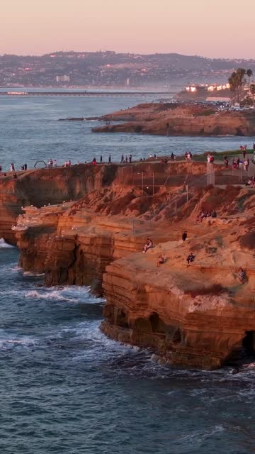 Low aerial view of the cliffs, palm trees and the ocean at Sunset Cliffs, with a crowd gathered.