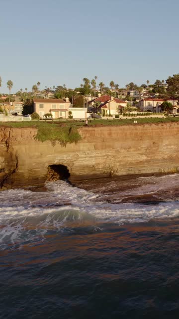 Low aerial view of the cliffs, the surf and palm trees at Sunset Cliffs.