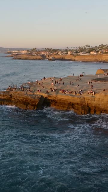 Aerial view of the cliffs, the surf and palm trees at Sunset Cliffs, with a crowd gathered.
