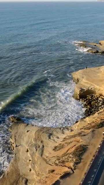 Aerial view of the cliffs, the surf and the ocean at Sunset Cliffs, with people walking.