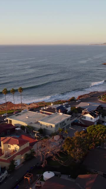 Aerial view of a residential street, the surf and palm trees at Sunset Cliffs, with people walking.