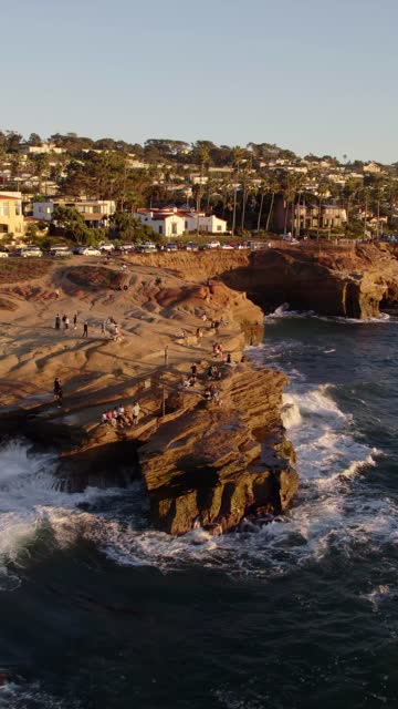 Low aerial view of the cliffs, the surf and palm trees at Sunset Cliffs, with people walking.