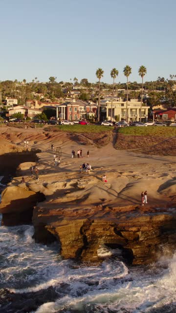 Low aerial view of the cliffs, the surf and palm trees at Sunset Cliffs, with people walking.