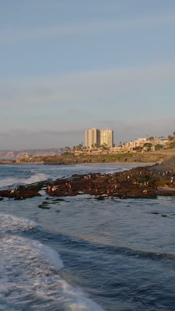 Low aerial view of the beach, the surf and the ocean at La Jolla Cove, with a crowd gathered.