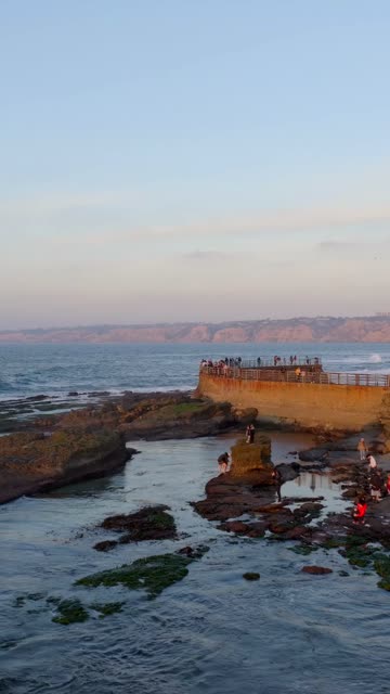 Low aerial view of the cliffs, the ocean and open country at La Jolla Cove, with a crowd gathered.