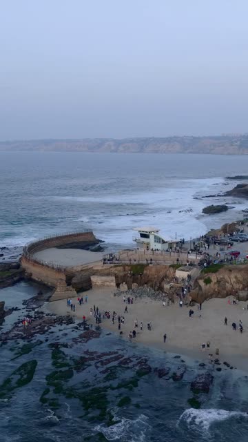 Aerial view of the cliffs, the surf and the ocean at La Jolla Cove, with a crowd gathered.