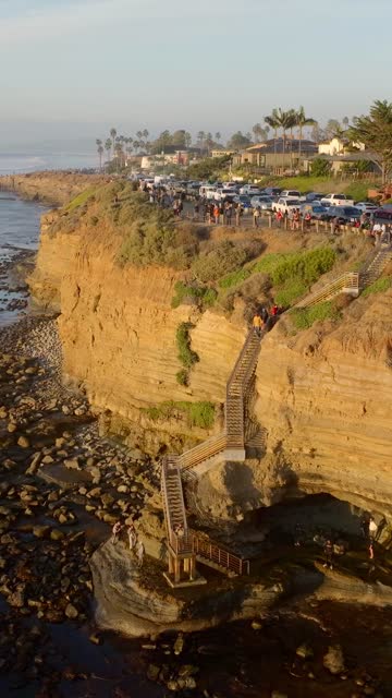 Aerial view of the cliffs, palm trees and the ocean at Sunset Cliffs, with a crowd gathered.
