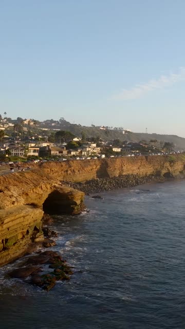 Low aerial view of the cliffs, palm trees and the ocean at Sunset Cliffs, with a crowd gathered.