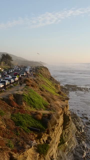 Aerial view of the cliffs, the surf and the ocean at Sunset Cliffs, with a crowd gathered.