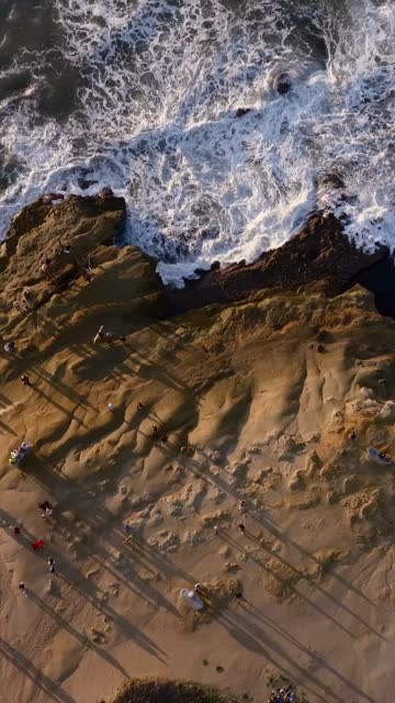 Aerial view of the cliffs, the surf and the ocean at Sunset Cliffs, with a crowd gathered.