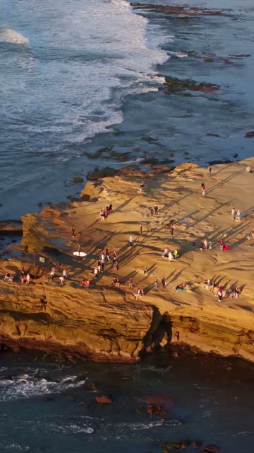 Aerial view of the cliffs, the surf and the ocean at Sunset Cliffs, with a crowd gathered.