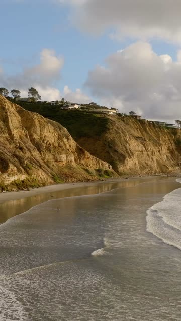 Low aerial view of the beach, the surf and the ocean at Black’s Beach, with people walking.