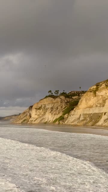 Low aerial view of the cliffs, the surf and the ocean at Black’s Beach.