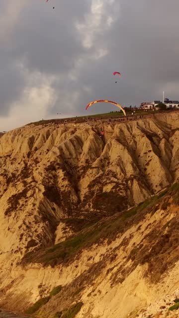 Low aerial view of the cliffs and open country at Black’s Beach, with a crowd gathered.