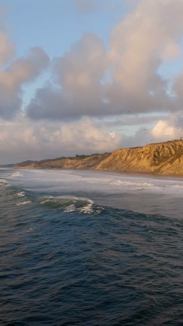 Low aerial view of the cliffs, the surf and the ocean at Black’s Beach.