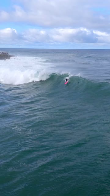 Low aerial view of the beach, the surf and the ocean at La Jolla Cove, with surfers out.