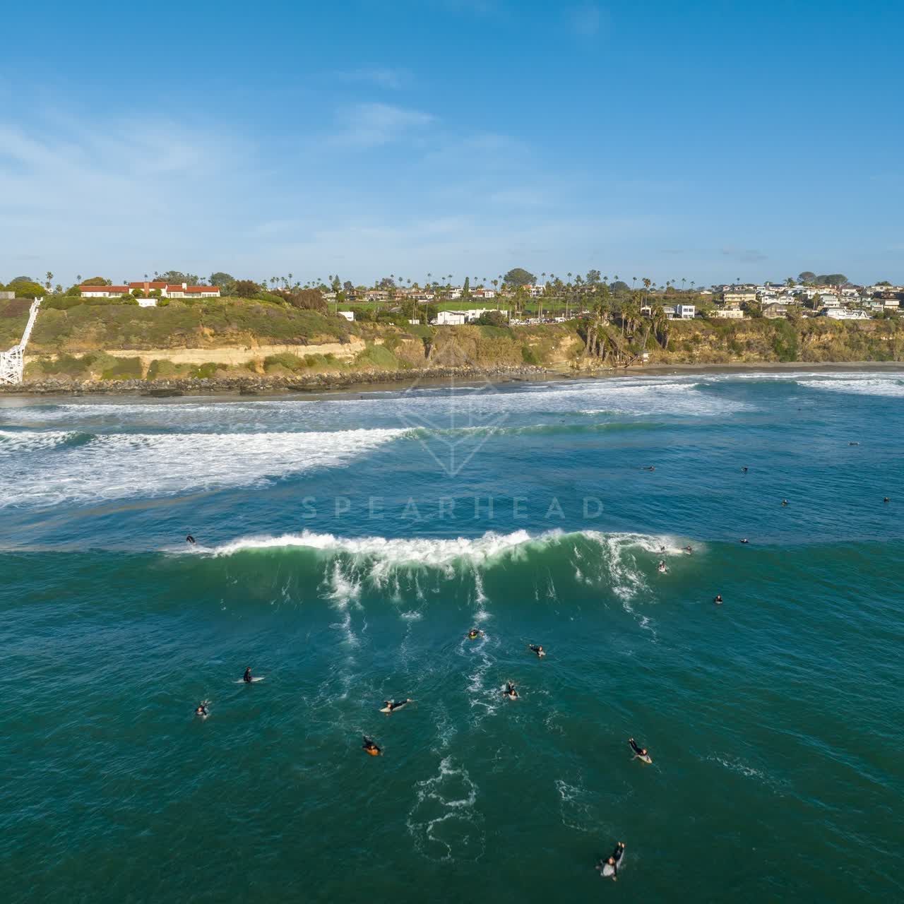 Low aerial view of the beach, the surf and palm trees at Swamis, with surfers out.