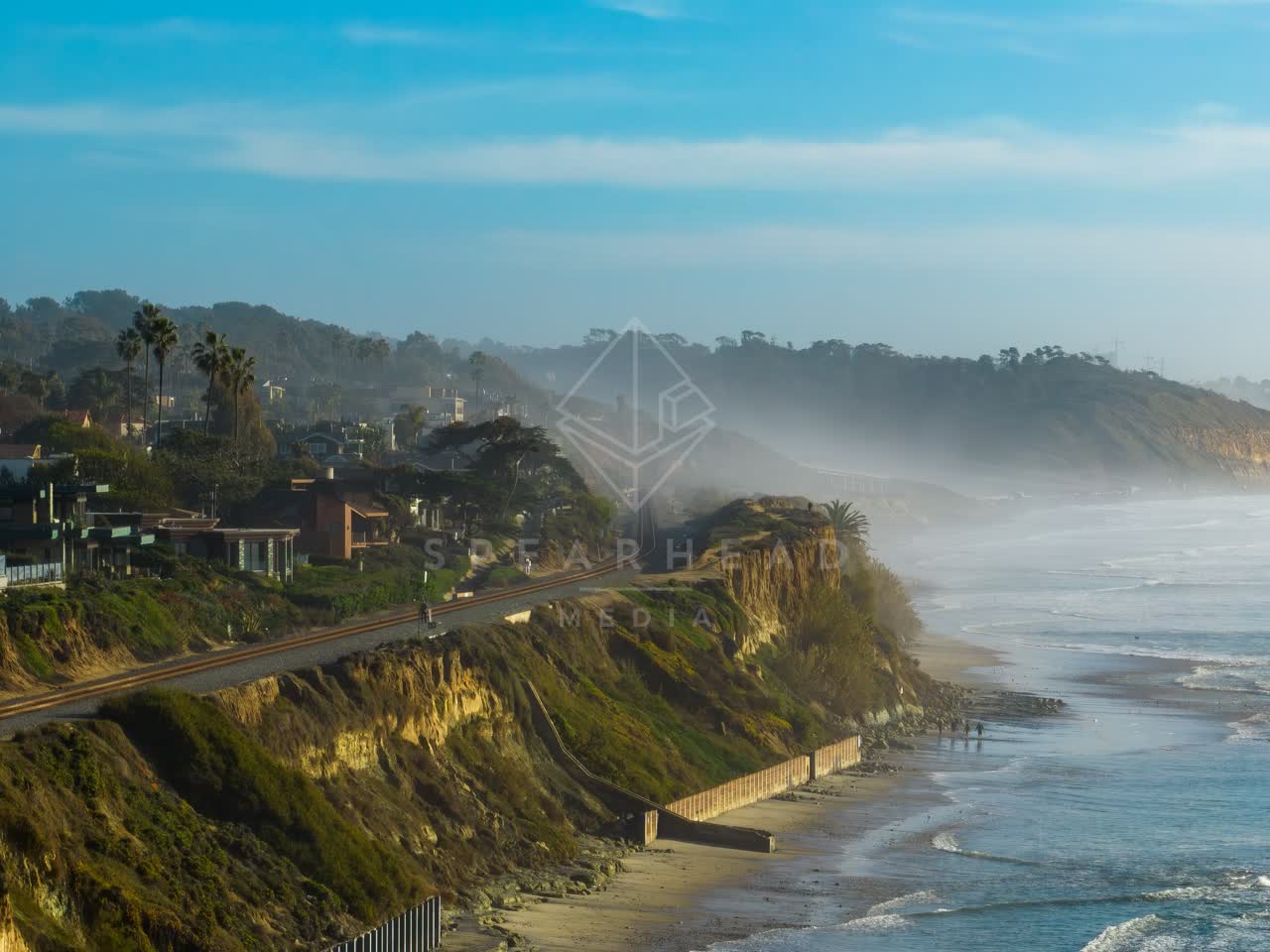 Aerial view of the cliffs, palm trees and the ocean in Del Mar, with people walking.