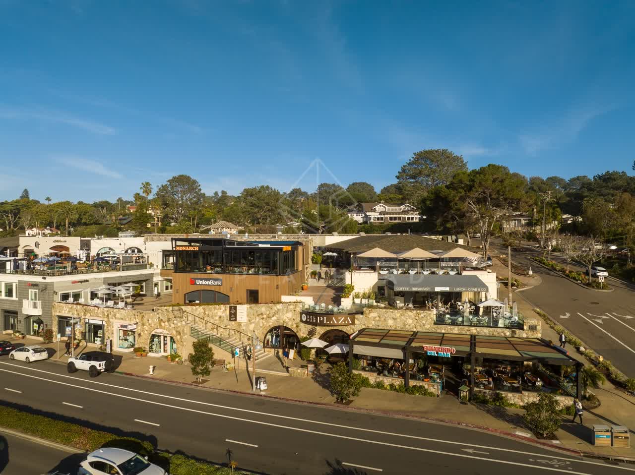 Low aerial view of the downtown streets, the buildings and traffic in Del Mar, with people eating outside.