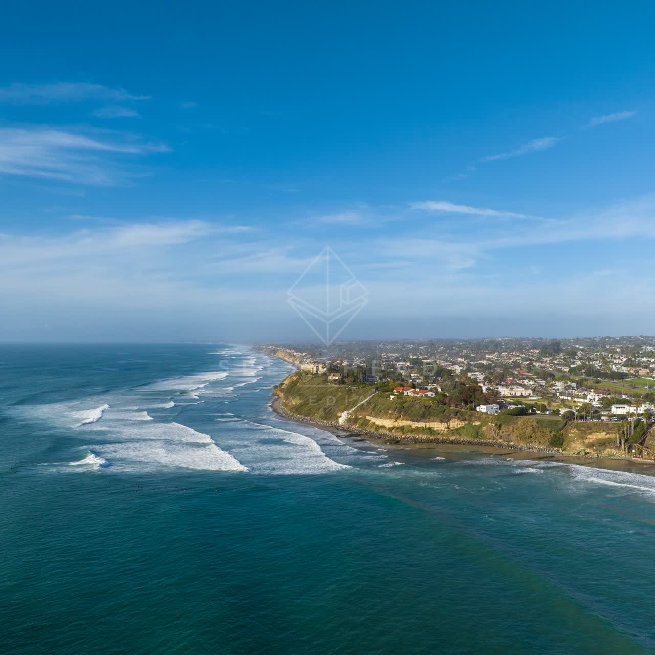 Aerial view of the cliffs, the surf and the ocean at Swamis, with surfers out.