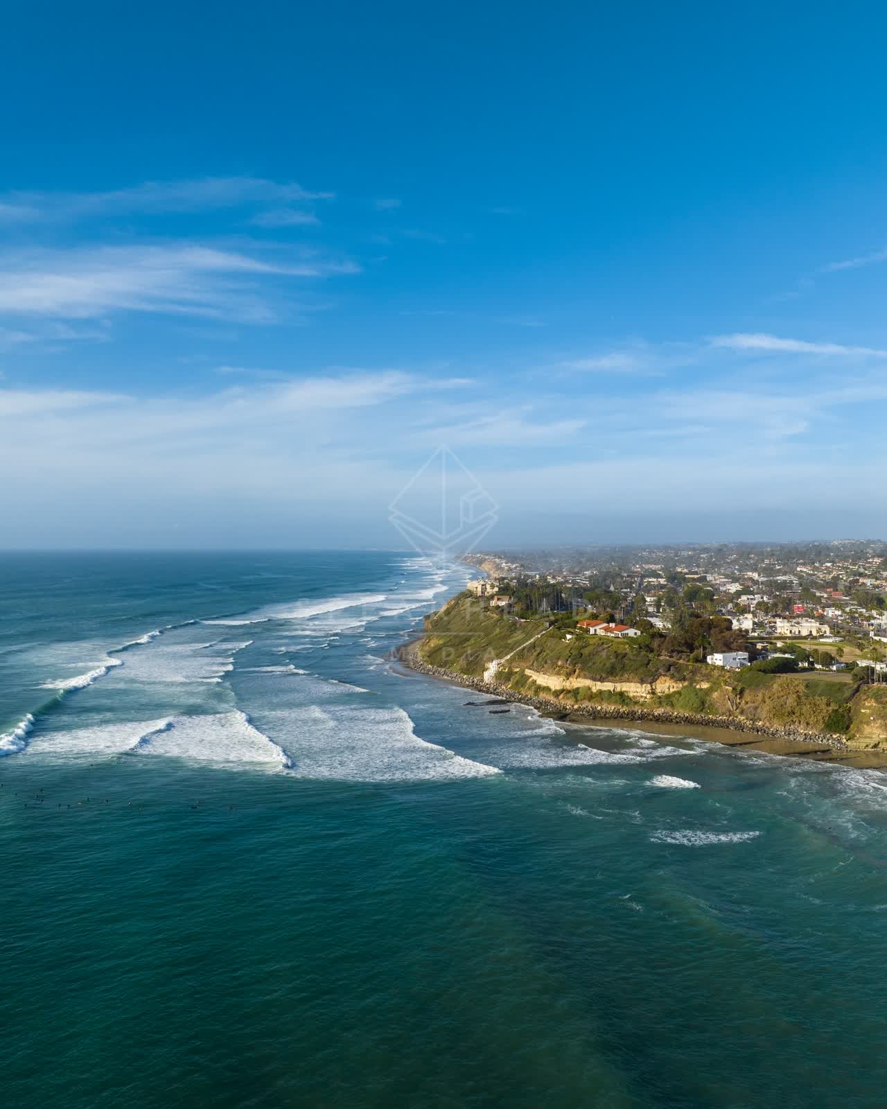 Aerial view of the cliffs, the surf and the ocean at Swamis, with surfers out.