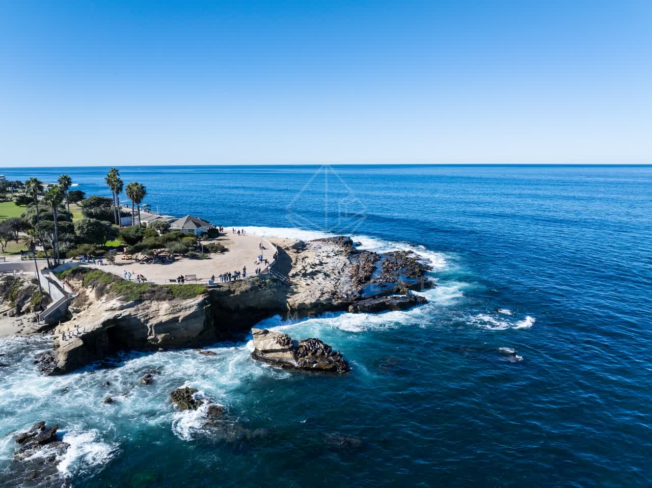 Aerial view of the cliffs, the surf and palm trees at La Jolla Cove, with people walking.