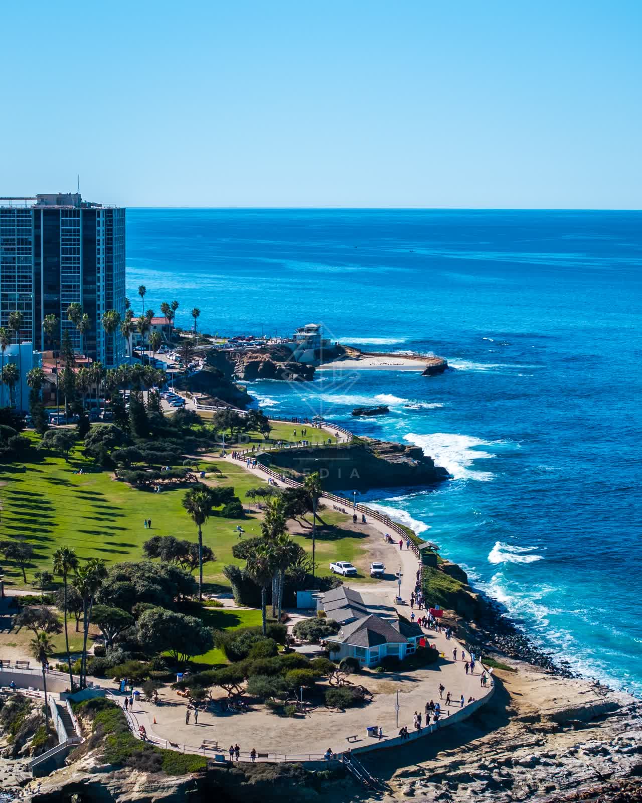 Aerial view of the cliffs, palm trees and the ocean at La Jolla Cove, with people walking.