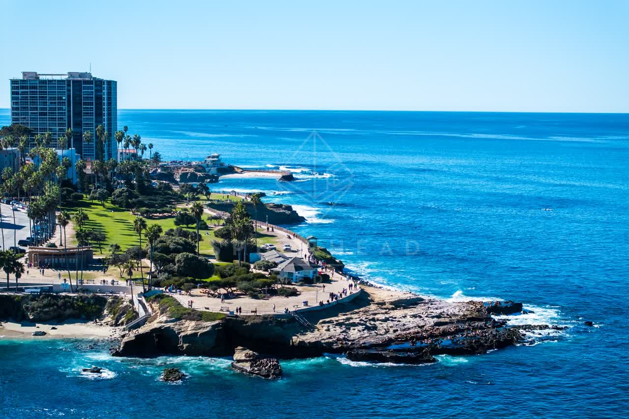 Aerial view of the cliffs, palm trees and the ocean at La Jolla Cove, with people walking.