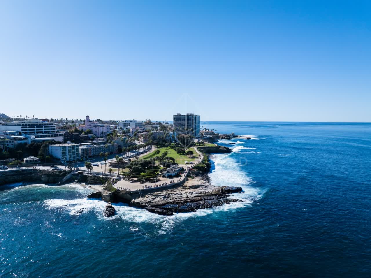 Aerial view of the cliffs, the surf and palm trees at La Jolla Cove, with people walking.