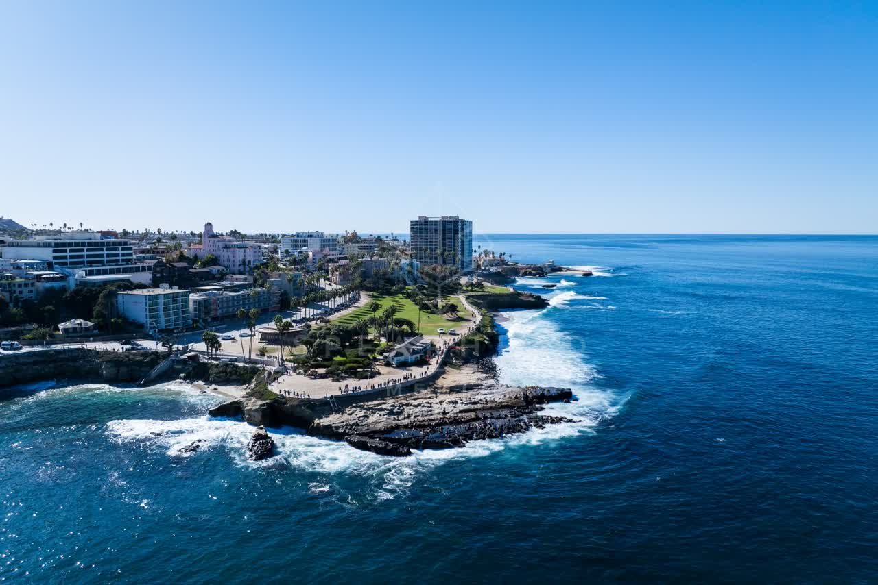 Aerial view of the cliffs, palm trees and the ocean at La Jolla Cove, with people walking.