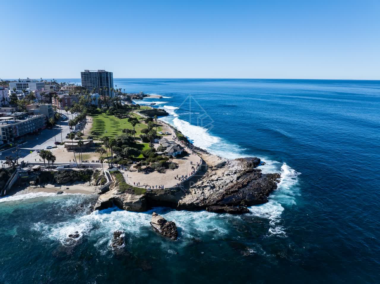 Aerial view of the cliffs, the surf and palm trees at La Jolla Cove, with people walking.