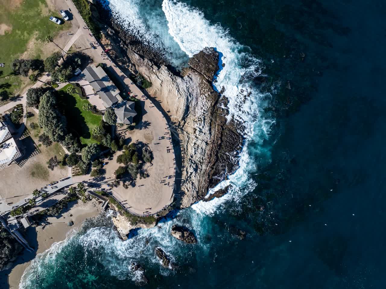Aerial view of the cliffs, the surf and the ocean at La Jolla Cove, with people walking.