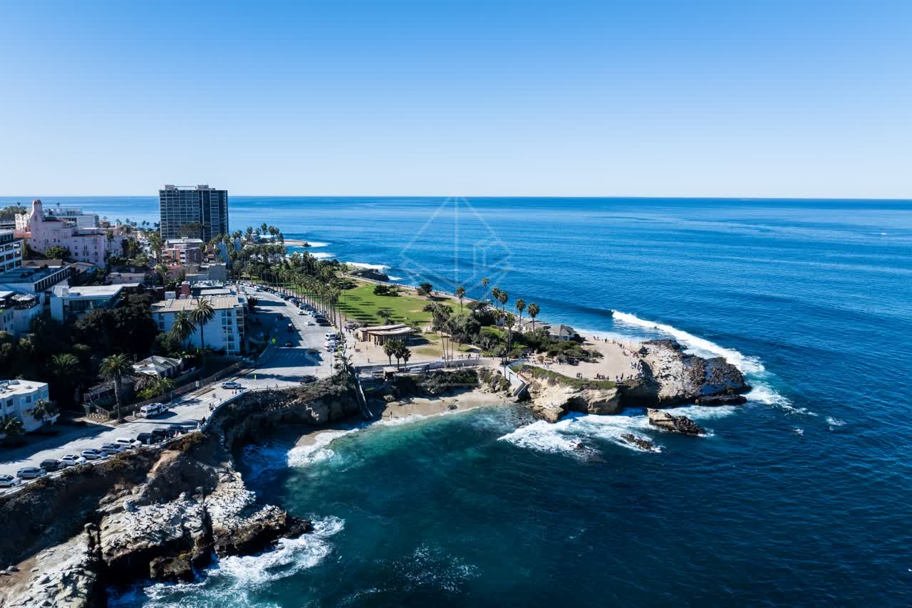Aerial view of the cliffs, palm trees and the ocean at La Jolla Cove, with people walking.
