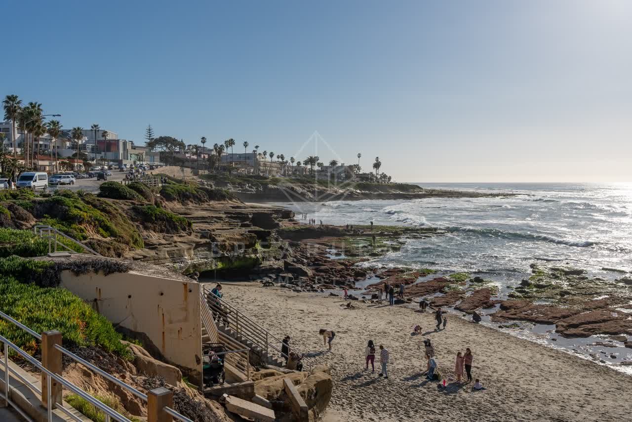Elevated view of the beach, the surf and palm trees at La Jolla Cove, with people walking.