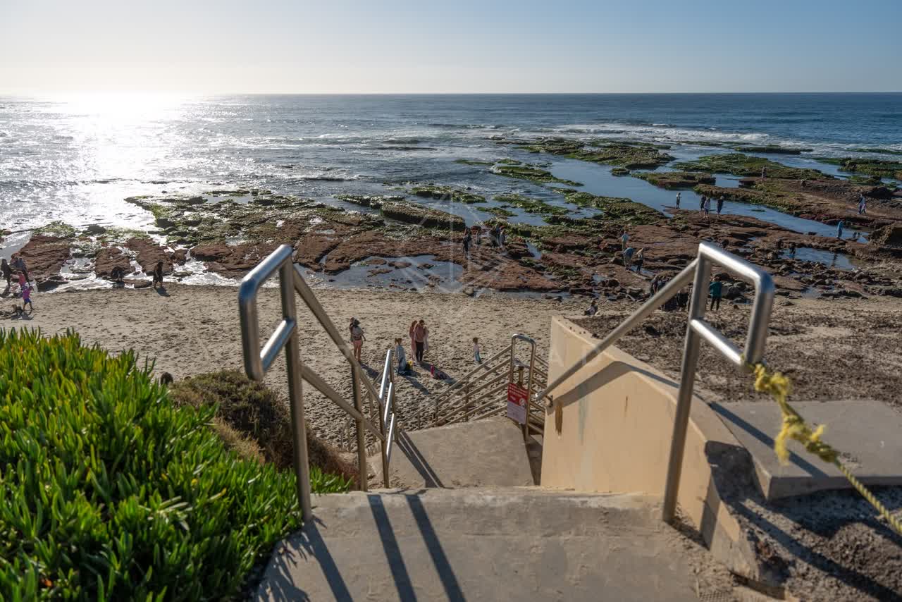 Elevated view of the beach, the ocean and the cliffs at La Jolla Cove, with people walking.