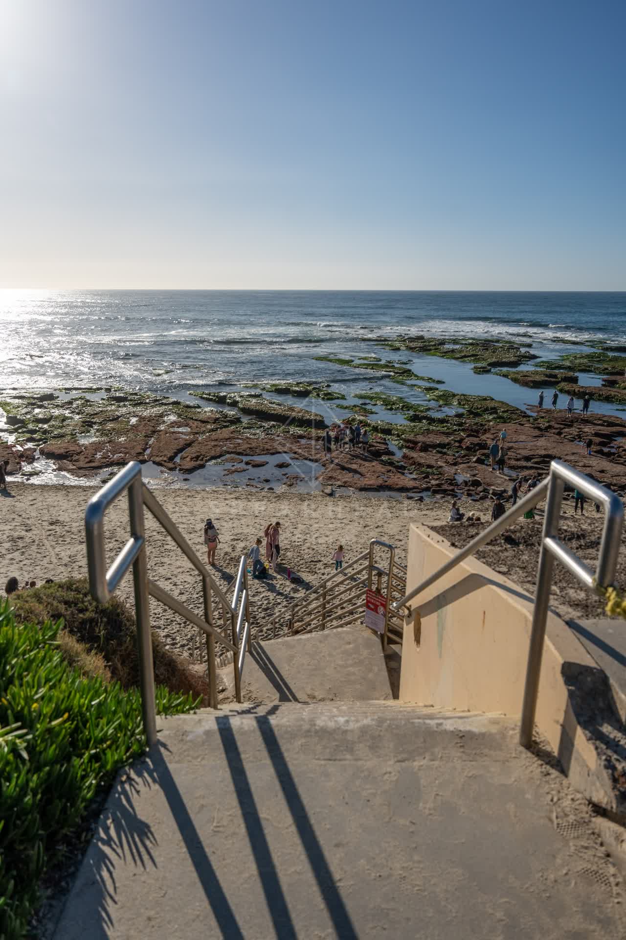 Elevated view of the beach, the ocean and the cliffs at La Jolla Cove, with people walking.
