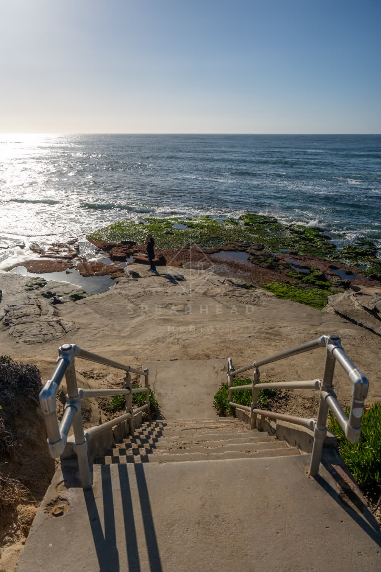 Elevated view of the cliffs, the ocean and the beach at La Jolla Cove, with people walking.